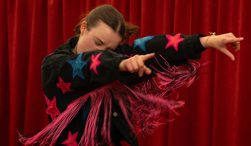 Bella Ramsey in una scena di 'Sunny dancer' mentre balla sul palco con un costume nero con frange rosa e stelle rosa e azzurre